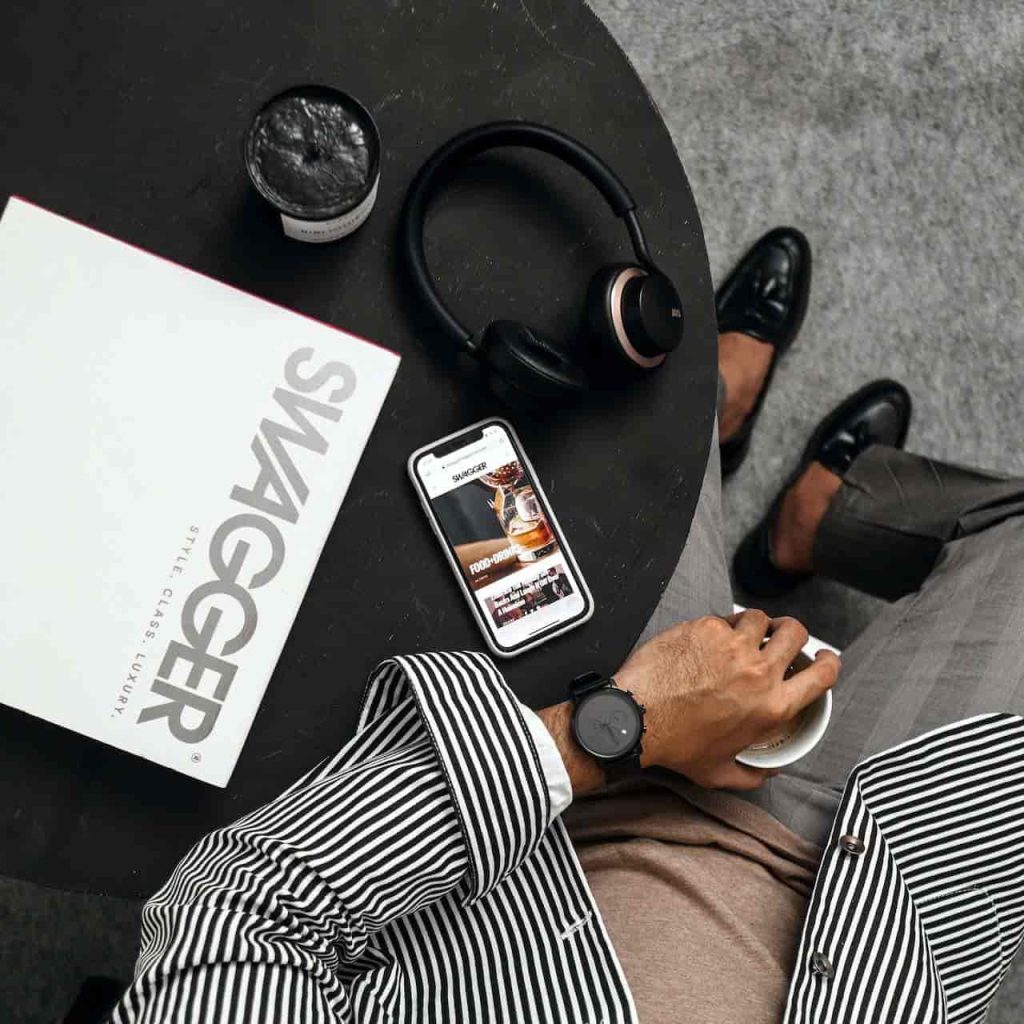 A successful business man sitting at a table with his gadgets and a Swagger magazine on top - NeoVisage.com